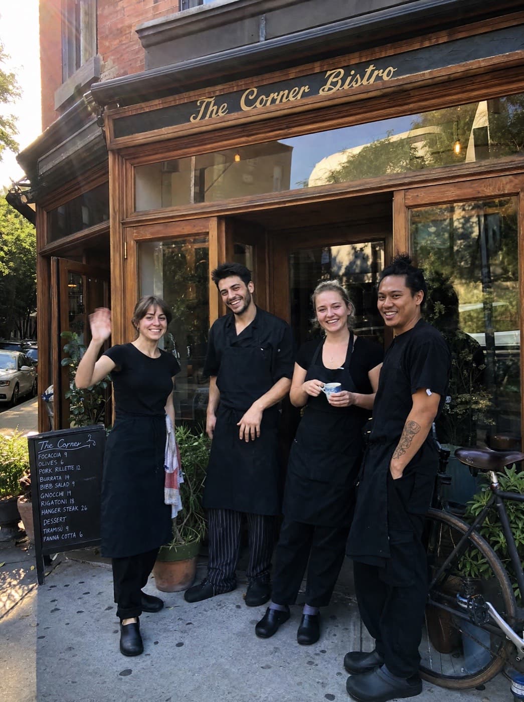 The Corner Bistro's storefront with four smiling team members in black aprons in front of the door.